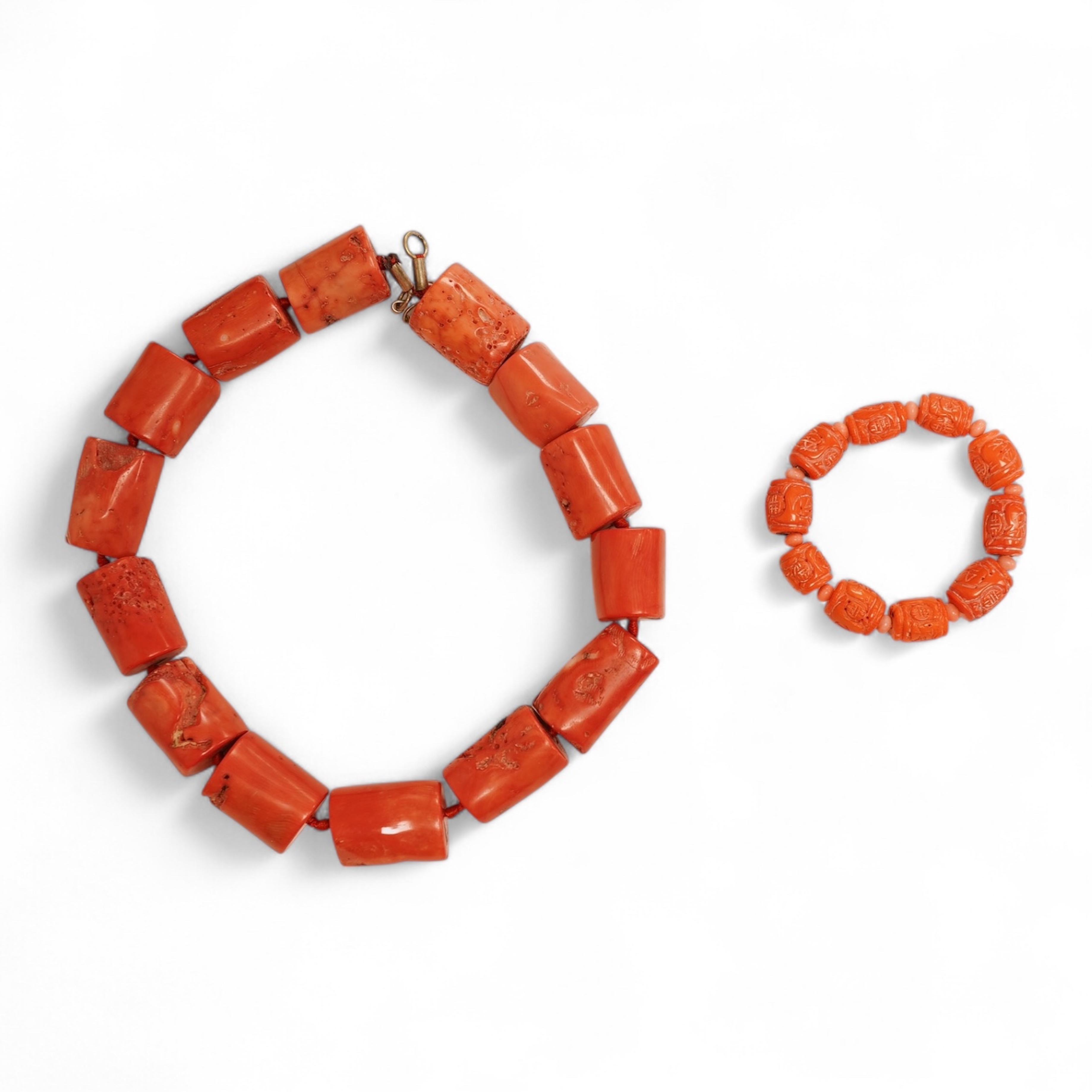 Two coral bead necklaces, one composed of large cylindrical coral beads, approximately 2.5-3.5cm each, total length 49cm; and a bracelet composed of carved coral beads spaced by smaller pink coral beads, on an elasticate